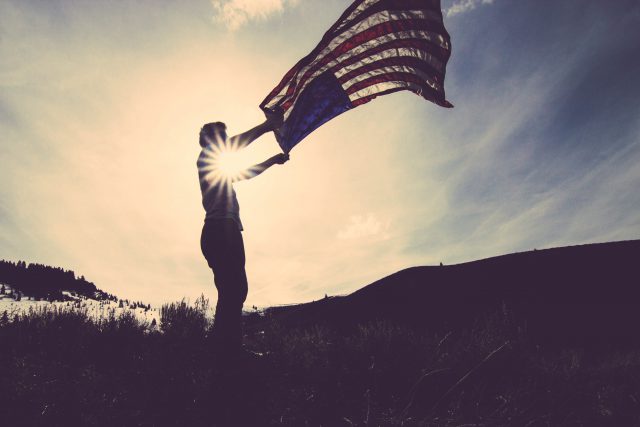 silhouette of someone holding an american flag with the sun on the background