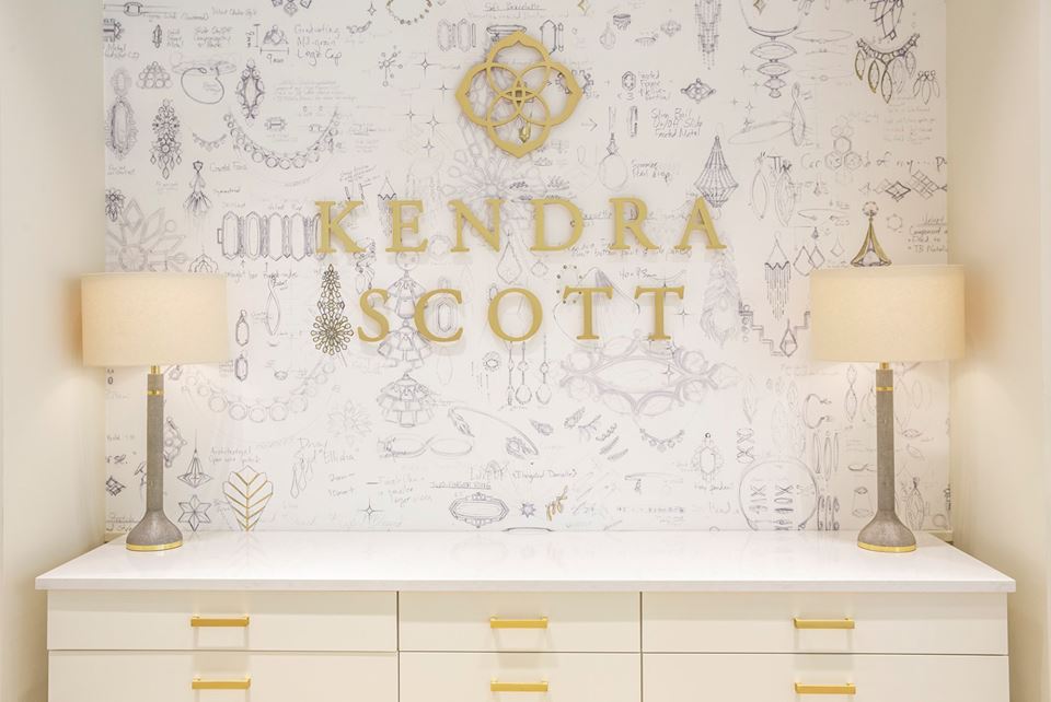 kendra scott logo on a white wallpaper wall with white/gold accessories and furniture