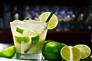 lime margarita with limes surrounding the cup and a blurry bar in the back