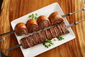 skewer of meats on a white plate with green garnish surrounding it