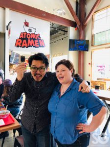 woman in a blue button up and a man in a black button up looking at the camera