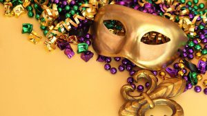 gold mardi gras mask with purple, yellow, and green beads/streamers and a yellow background