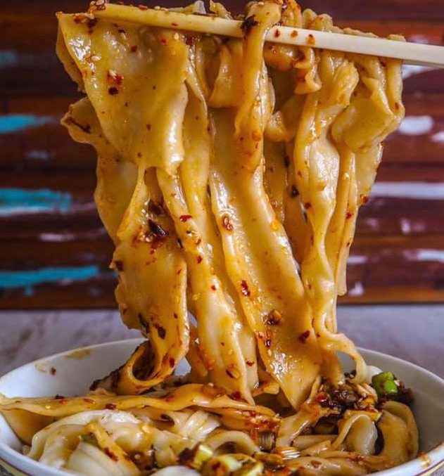 Biang Biang Noodles with a sauce and other ingredients being lifted by chop sticks