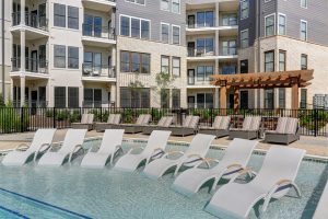 The Henry: lounge chairs in the shallow end of a pool and apartment complex in the background