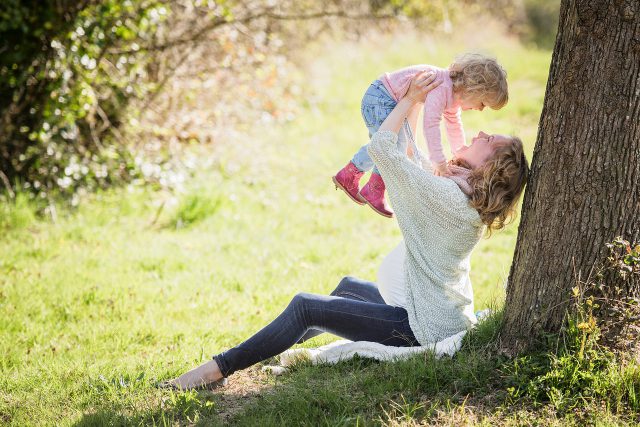Mother's Day: woman holding her baby over her head leaning against a tree