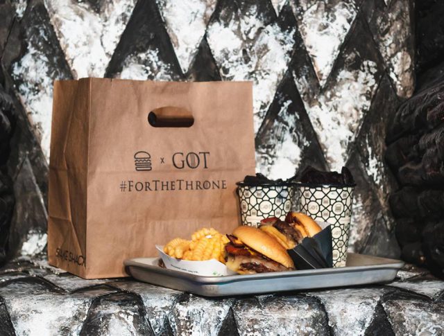 Game of Thrones: a brown bag that says GoT and a burger meal on a tray sitting on a metal chair
