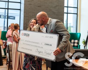 Origin Hotel: two people holding a big check while a dog "kisses" the man