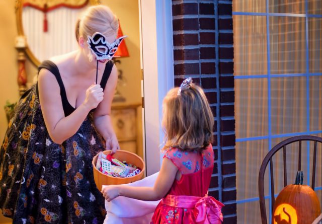 LCA: a woman in a halloween cosutme giving candy to a girl in a halloween costume