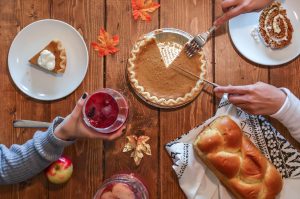 Thanksgiving: table with pumpkin pie, bread, a drink, and hands